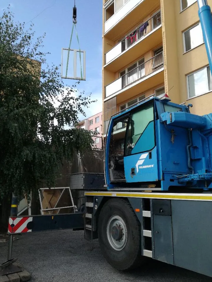 Žeriav zdvíha zabalenú presklenú výplň pozdĺž fasády